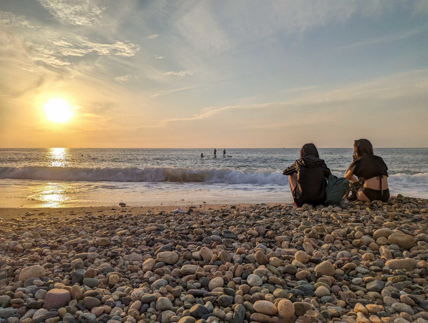 a couple of people sitting on top of a rocky beach.