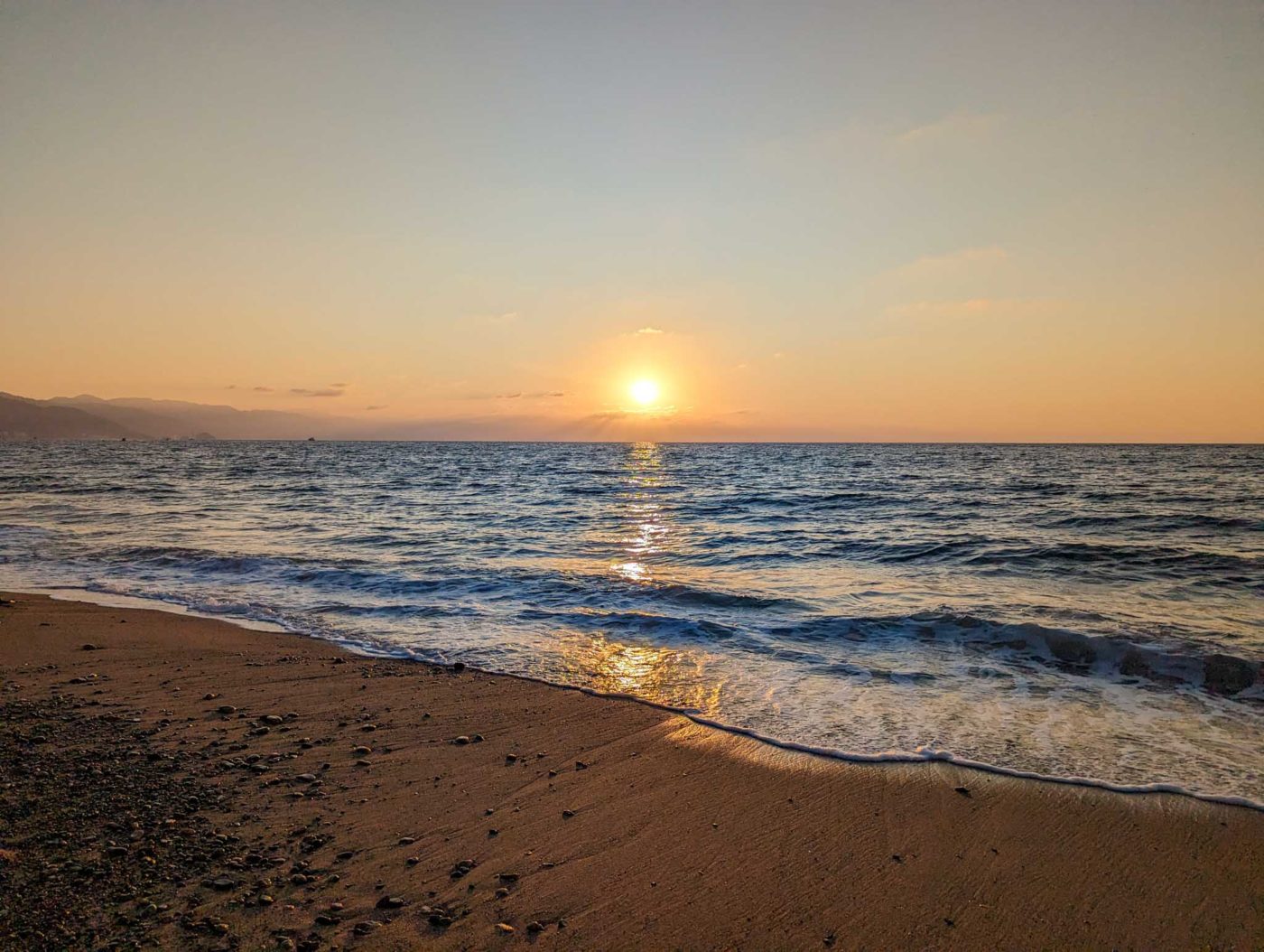 the sun is setting over the water on the beach.