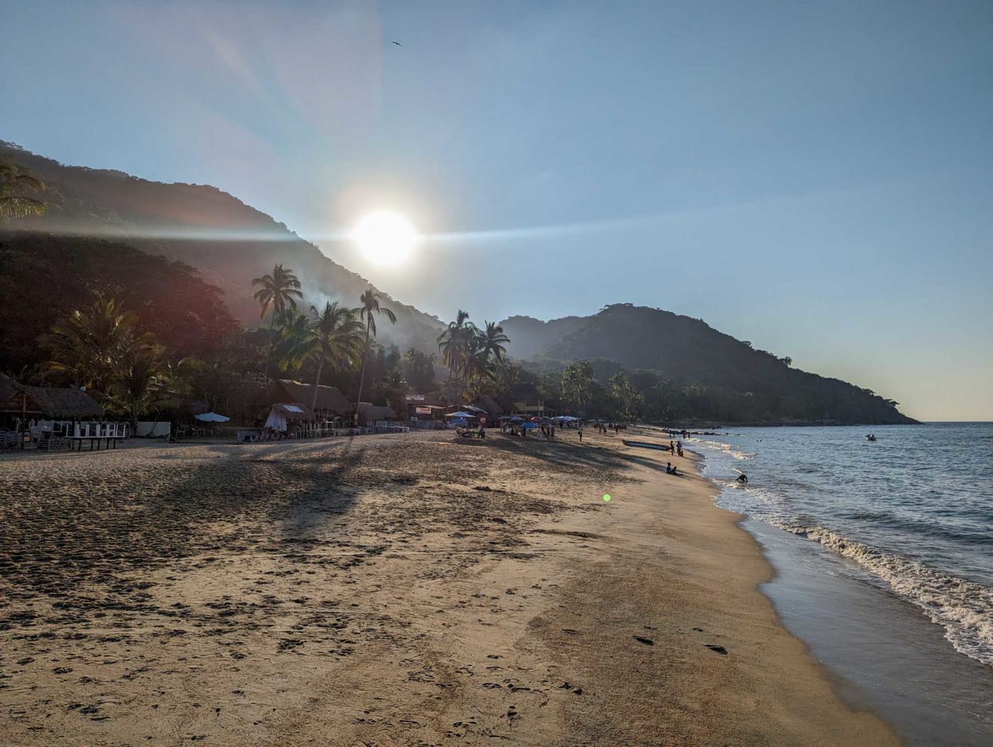 the sun is shining over a beach with a mountain in the background.