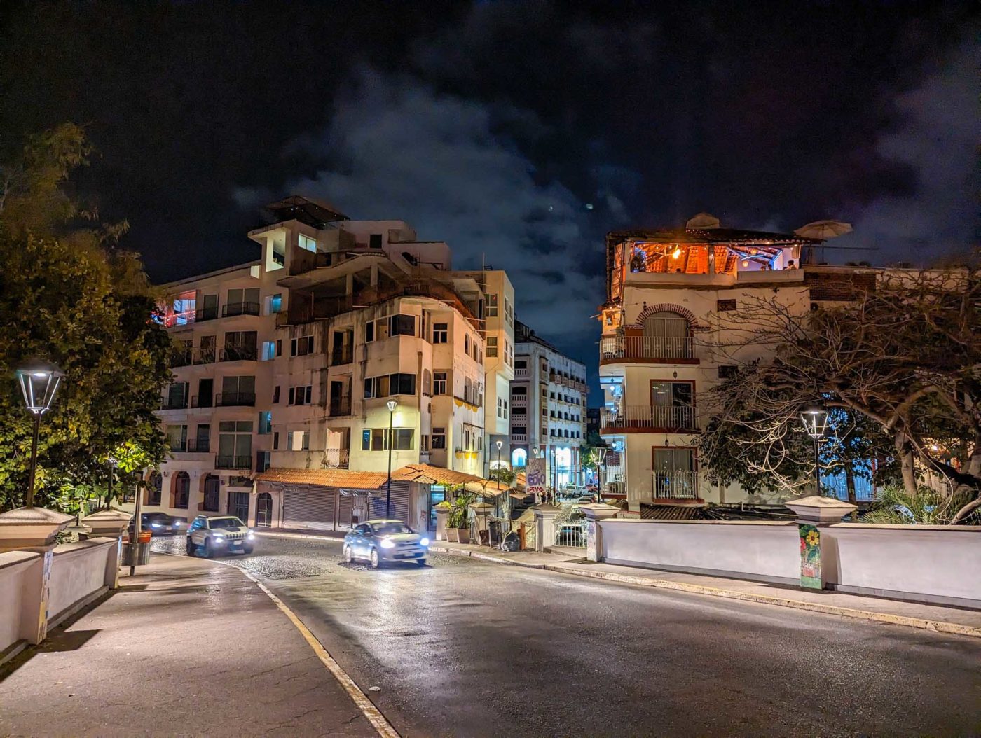 a city street at night with cars parked on the side of the road.